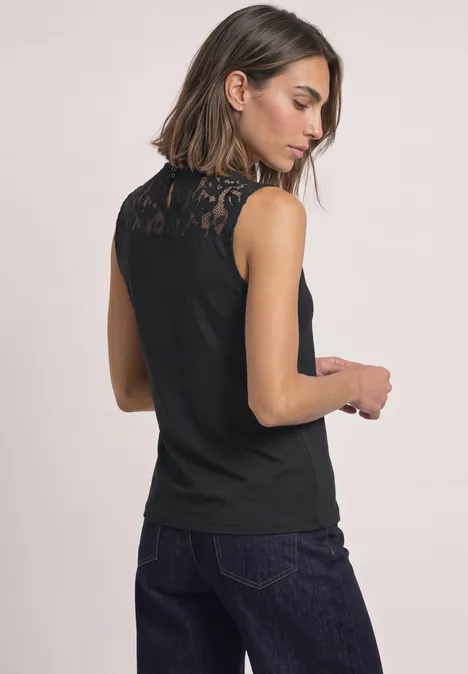 Frau von hinten in ärmellosem schwarzen Spitzen-Top und dunkler Jeans.