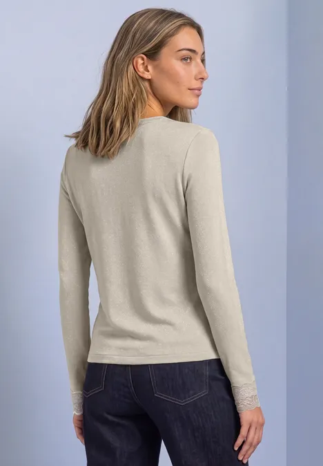 Shirt met glitters en kant pure beige Vrouw gezien van achteren in een beige longsleeve en donkere jeans voor een neutrale achtergrond.