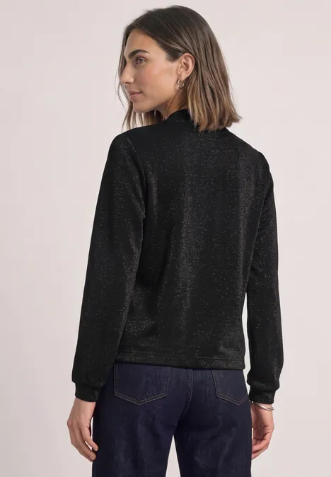 Leichter Blouson mit Glitzerdetails Black Frau von hinten in funkelndem schwarzen Pullover und blauer Jeans vor hellem Hintergrund
