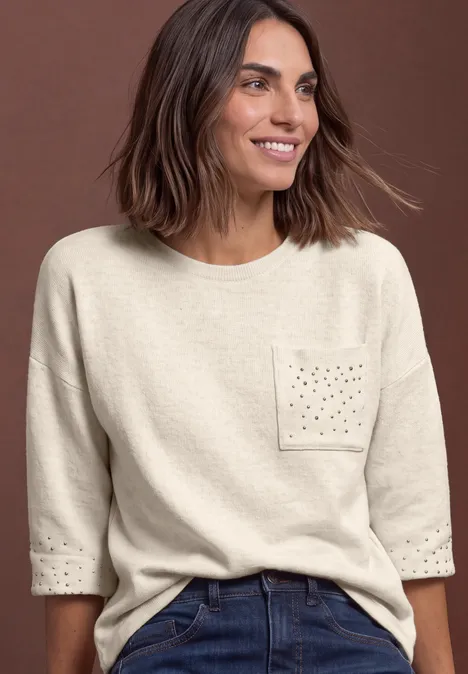Shirt met 3/4-mouwen en siersteentjes clay sand mel. Eine lächelnde Frau mit braunen Haaren trägt einen hellbeigen Pullover mit dekorativer Brusttasche.