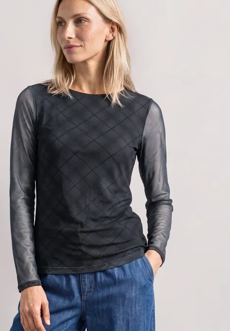 Langarm Shirt aus Mesh mit Karomuster armor grey Frau in durchsichtigem schwarzen Langarmshirt mit Karomuster und blauer Jeans vor hellem Hintergrund.