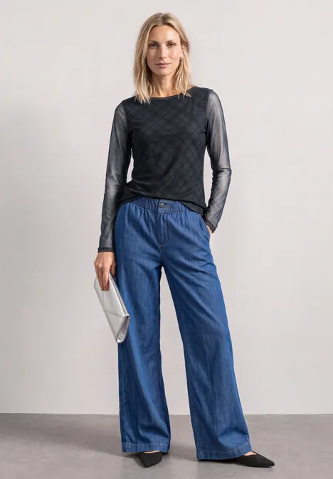 Langarm Shirt aus Mesh mit Karomuster armor grey Eine Frau in schwarzem Mesh-Oberteil, weiten Jeans und schwarzen Schuhen mit silberner Clutch.