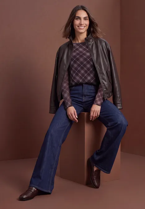 Femme en veste en cuir sur les épaules, pull à carreaux, jeans taille haute évasés et bottines marron.