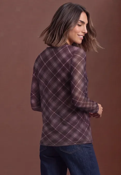 Femme de dos en chemise à carreaux violette et jean, souriante, regardant de côté.