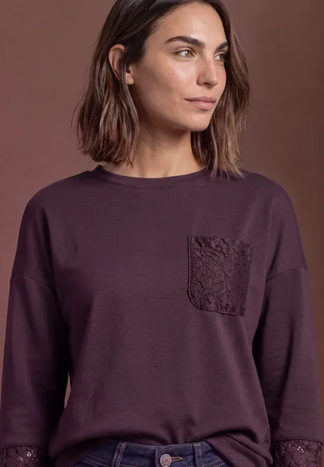 Sweat-shirt à détails dentelle berry plum Frau mit schulterlangem Haar trägt ein dunkelviolettes Langarmshirt mit dekorativer Brusttasche.