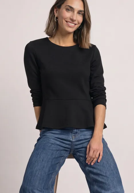 Langarm Shirt mit Volant-Saum Black Frau in schwarzer Langarmbluse mit tailliertem Saum und blauen Jeans posiert lächelnd.