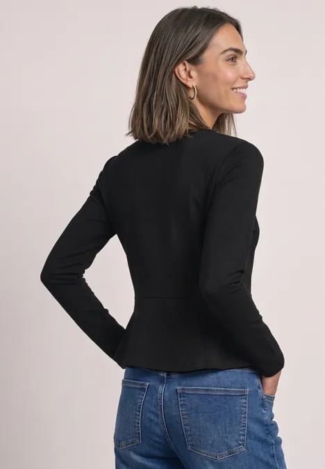 Langarm Shirt mit Volant-Saum Black Frau trägt schwarzen, taillierten Blazer mit langen Ärmeln, steht seitlich abgewandt und lächelt.