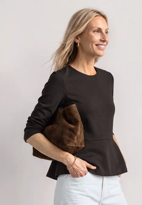 Langarm Shirt mit Volant-Saum black coffee Frau in schwarzem Peplum-Top und weißen Hosen, lächelt und hält eine braune Clutch vor hellem Hintergrund.