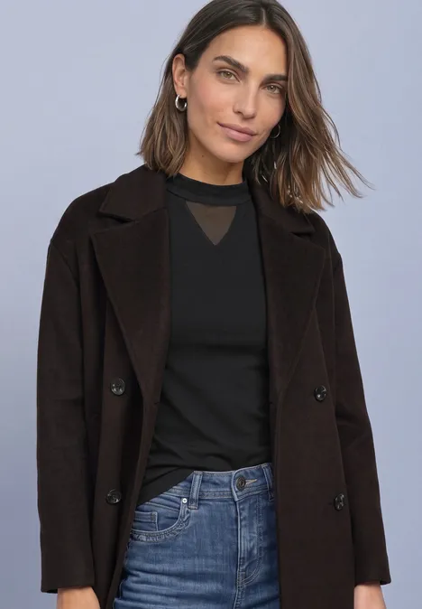 Shirt met lange mouwen, col en mesh-detail Black Junge Frau in schwarzem Top, dunklem Mantel und Jeans vor neutralem Hintergrund.