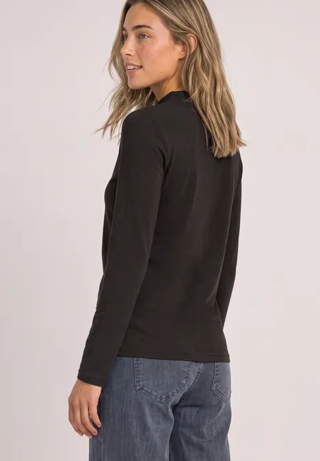 Shirt met lange mouwen, col en mesh-detail black coffee Een jonge vrouw in profiel, zwarte trui, blauwe jeans, kijkt over haar schouder.