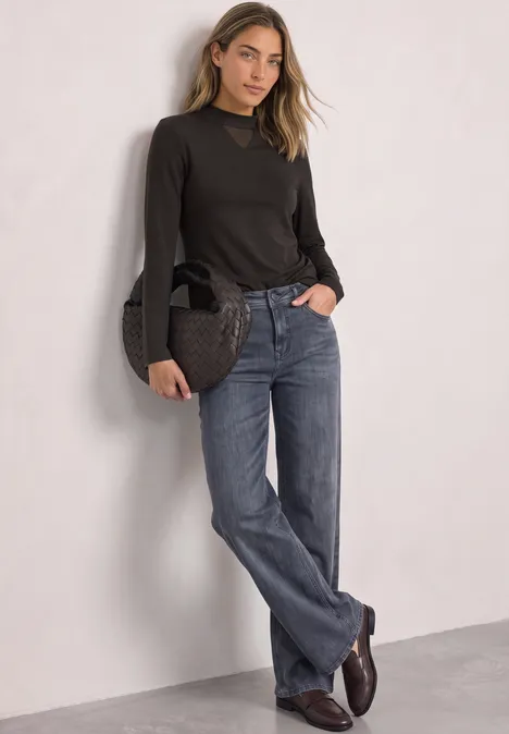 Shirt met lange mouwen, col en mesh-detail black coffee Vrouw in donkerbruin shirt en blauwe jeans leunt tegen lichte muur en houdt een handtas vast.