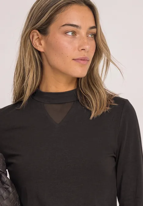 Shirt met lange mouwen, col en mesh-detail black coffee Vrouw met halflang haar in zwart T-shirt met lange mouwen, kijkt zijdelings in een rustig portret.