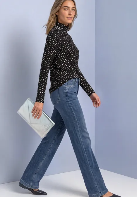 Eenvoudig shirt met col en patroon Black Vrouw draagt zwarte blouse met stippen, rechte blauwe jeans en zilverkleurige clutch voor lichte achtergrond.
