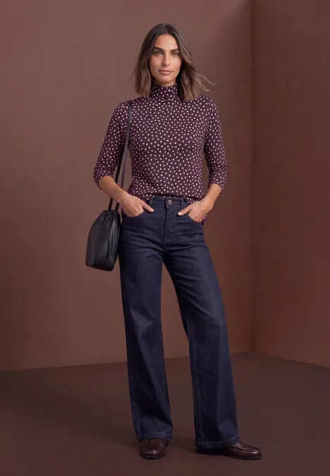 Basic Shirt mit Rollkragen und Muster berry plum Frau im gepunkteten Rollkragenpullover, weiten Jeans und schwarzer Schultertasche vor neutralem Hintergrund.
