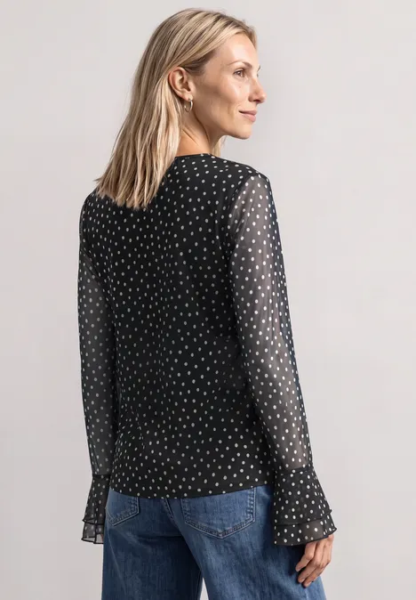Shirt aus Mesh mit Print und Volantdetails Black Frau in schwarzer, transparenter Tupfenbluse und blauer Jeans, steht seitlich zum Betrachter.