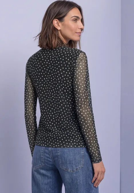 Shirt aus Mesh mit Turtle Neck und Print Black Frau im Profil mit schwarzem, gepunktetem Mesh-Langarmshirt und blauer Jeans.