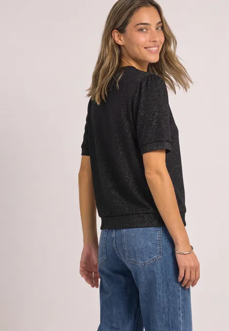 Kurzarm Jacke mit Rundhals und Glitzer Black Eine lächelnde junge Frau in schwarzem T-Shirt und blauen Jeans blickt über die Schulter.