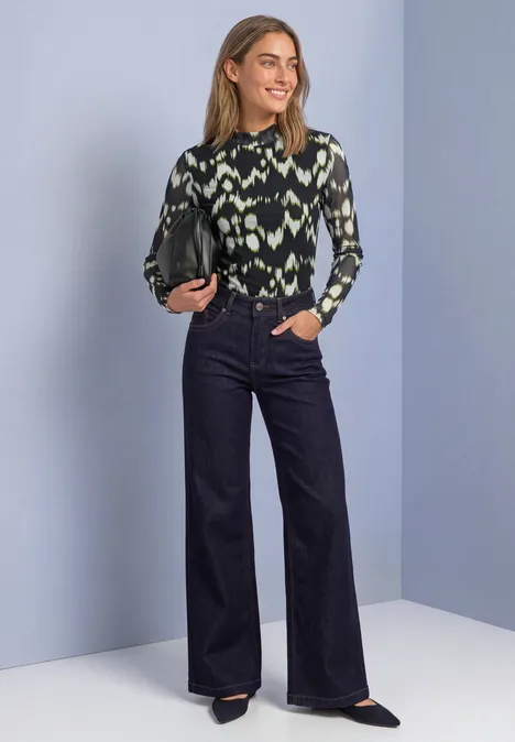 Shirt van mesh met col en print Black Frau in grün gemustertem Oberteil und hoch taillierter, weiter dunkler Jeans.