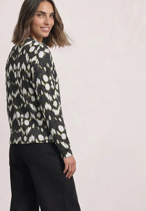 Shirt mit Turtle Neck und Tunnelzug Black Frau in schwarz-weiß gemustertem Pulli und schwarzer Hose, die zur Seite blickt und lächelt.