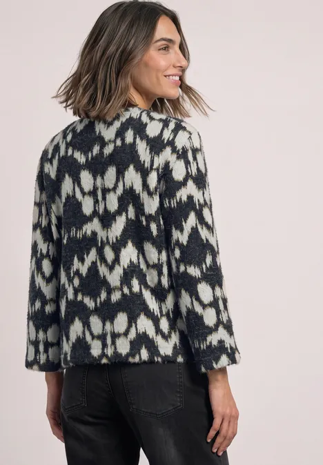 Une femme vue de dos porte une veste noire et blanche à motif ikat, se retournant et souriant.