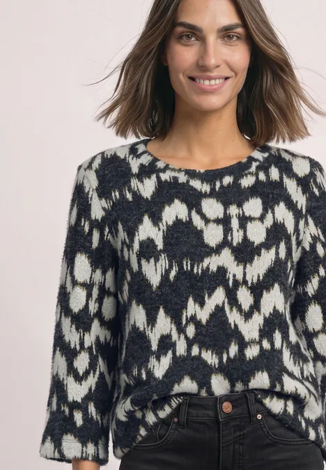 Femme souriante portant un pull noir et blanc à motifs.