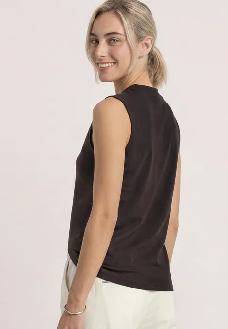 Basic top espresso brown Junge Frau mit blondem Pferdeschwanz, ärmellosem schwarzem Top und weißer Hose schaut lächelnd über die Schulter.
