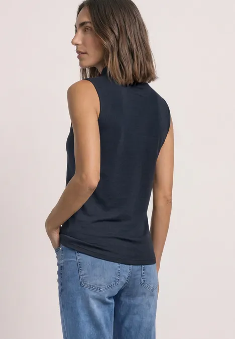Basic top shadowed navy Vrouw in donkerblauw mouwloos shirt en jeans, zijwaarts, hand in zak.