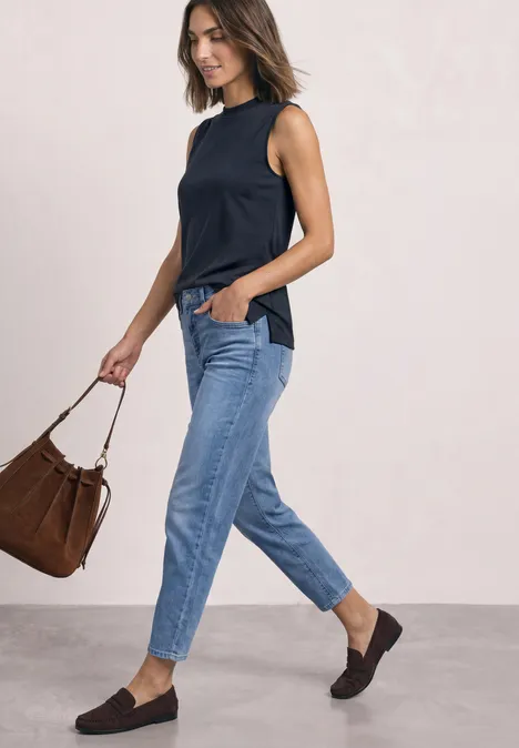 Basic top shadowed navy Vrouw in zwarte top, blauwe jeans en zwarte loafers, met bruine tas, lopend.