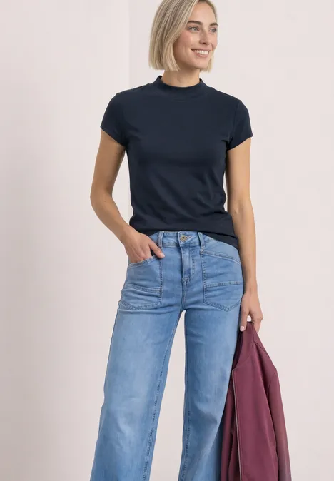 Basic Shirt mit Turtle Neck shadowed navy Frau lacht, trägt dunkelblaues T-Shirt, helle Jeans und hält eine lila Jacke.