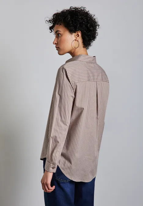 Frau mit lockigem Haar, gestreiftem Hemd und Jeans steht seitlich.