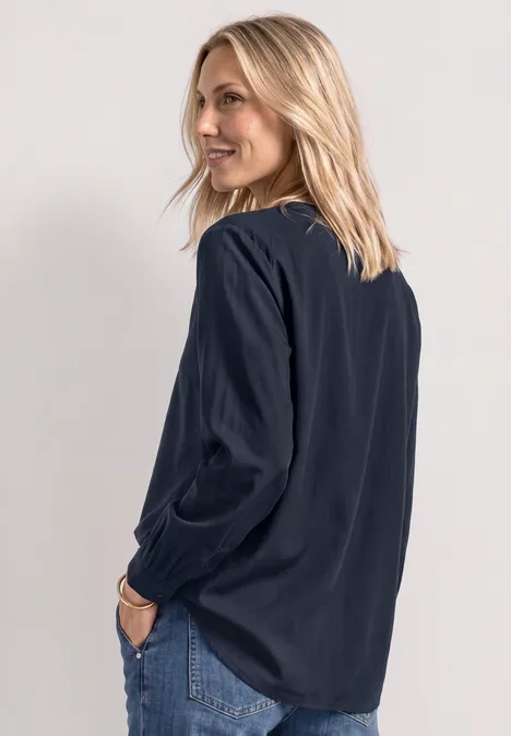Split Neck Tunika darkest blue Eine Frau mit blonden Haaren trägt eine dunkelblaue Bluse und Jeans, schaut lächelnd über die Schulter.