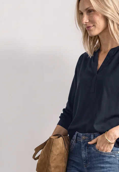 Split Neck Tunika darkest blue Frau in dunkelblauem Oberteil und Jeans, mit hellbrauner Tasche seitlich