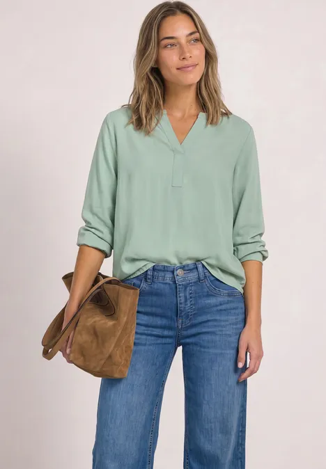 Vrouw in mintgroene blouse en jeans met een bruine tas