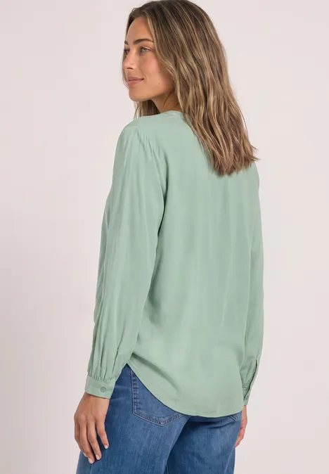 Vrouw in een lichtgroene blouse met lange mouwen, licht van opzij gefotografeerd.