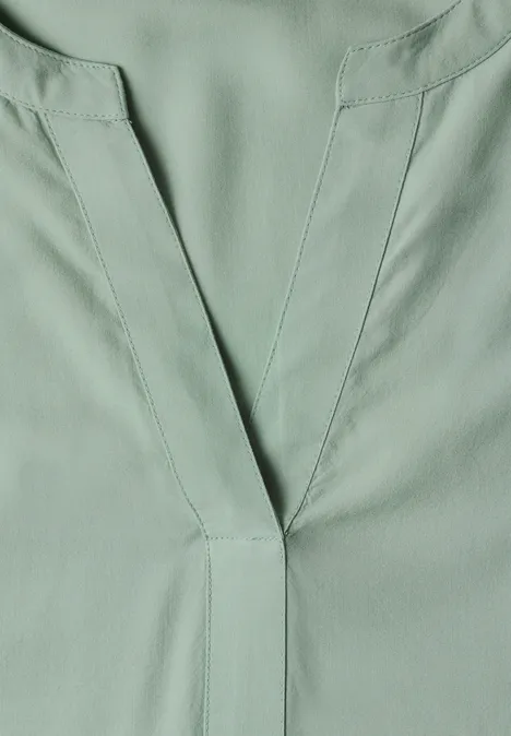 Close-up van een lichtgroene top met V-hals van soepelvallende stof
