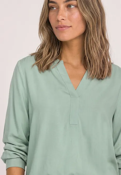 Bovenlichaam van vrouw in lichtgroene V-hals blouse met opgerolde mouwen en golvend haar.