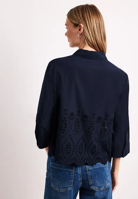 Achteraanzicht van een vrouw in donkerblauw jasje met driekwartmouwen en bloemenborduursel.