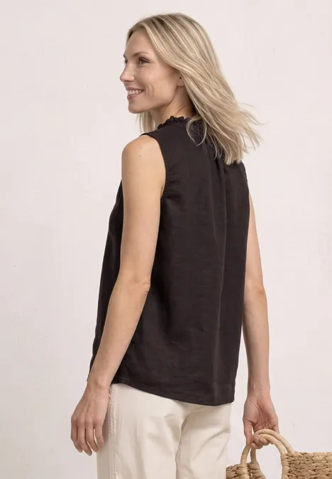 Frau von hinten in schwarzem ärmellosem Top und hellen Hosen, trägt einen Strohkörbchen, blonde Haare.