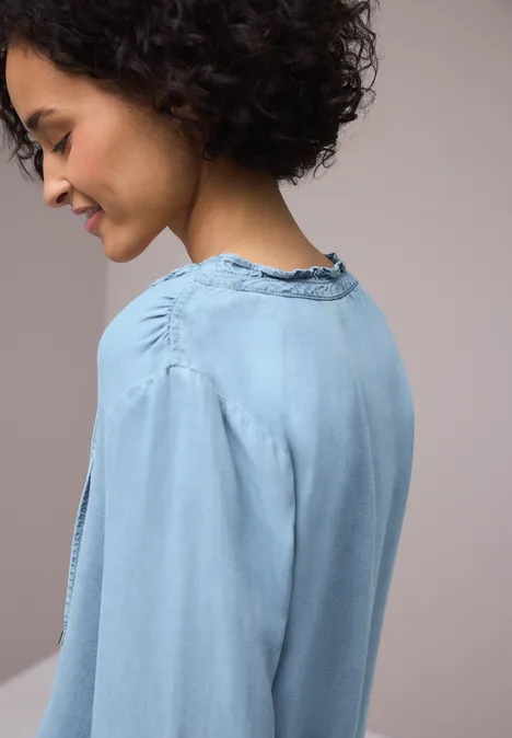 Zijaanzicht van een persoon met donker krullend haar in een lichtblauwe spijkerblouse.