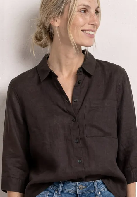 Femme en chemise en lin brun foncé à manches 3/4 et jean sur fond clair.