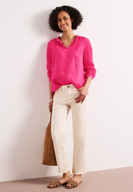 Dame in felroze blouse, lichte broek, sandalen en bruine tas voor een witte achtergrond.