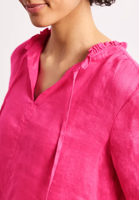 Een persoon draagt een felroze linnen blouse met V-hals en gerimpelde kraag.