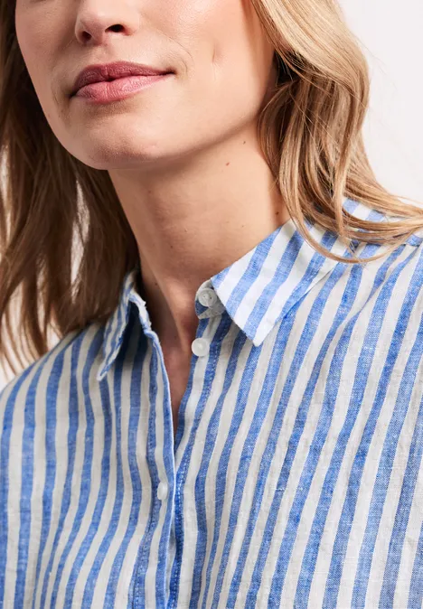 Close-up van een vrouw in een blauw-wit gestreept linnen overhemd met open kraag.