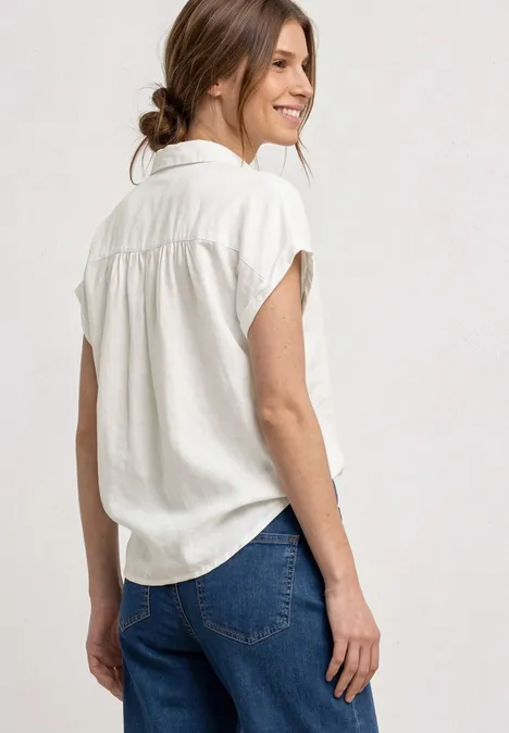 Persoon van achteren met wit kort mouw overhemd en blauwe jeans, haar losjes in een knot.