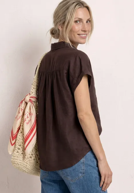 Vrouw van achteren in een bruin shirt en spijkerbroek, met een strooien tas en rood-witte sjaal.