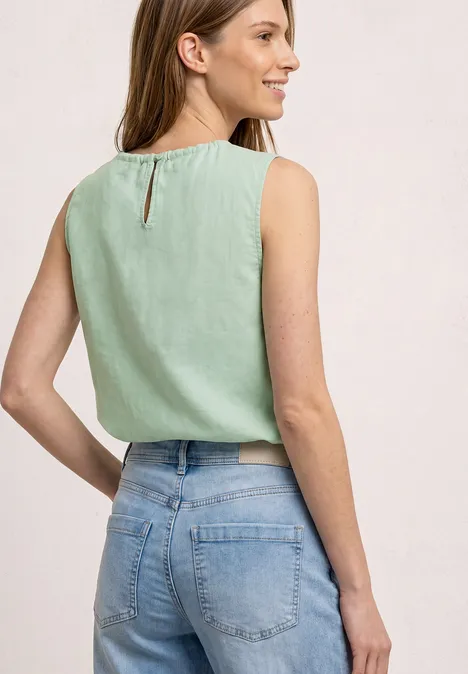 Eine Frau von hinten trägt ein ärmelloses mintgrünes Top und helle Jeans.