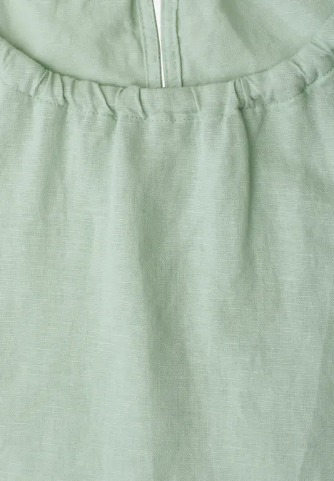 Nahaufnahme eines hellgrünen Leinenoberteils mit Raffung am Ausschnitt und Reißverschluss