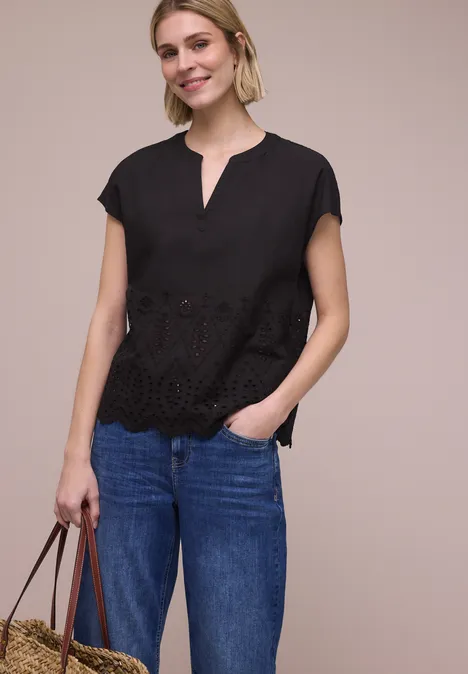 Vrouw in zwarte blouse met ajourdetails en blauwe jeans, met een handtas in de hand.