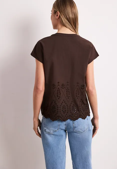 Vrouw van achteren in bruin T-shirt met geperforeerde zoom en blauwe spijkerbroek.