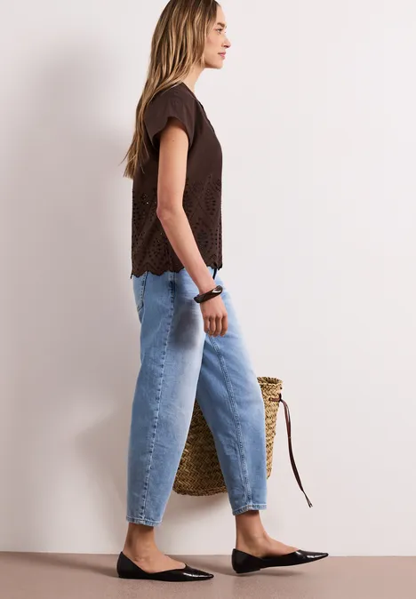 Zijaanzicht van een vrouw in spijkerbroek, zwart shirt, ballerina's en strooien tas.